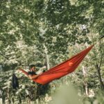 man on red hammock surrounded by trees during daytime
